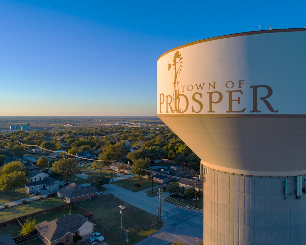 Town of Prosper water tower with the town name and windmill logo overlooking neighborhoods at sunset
