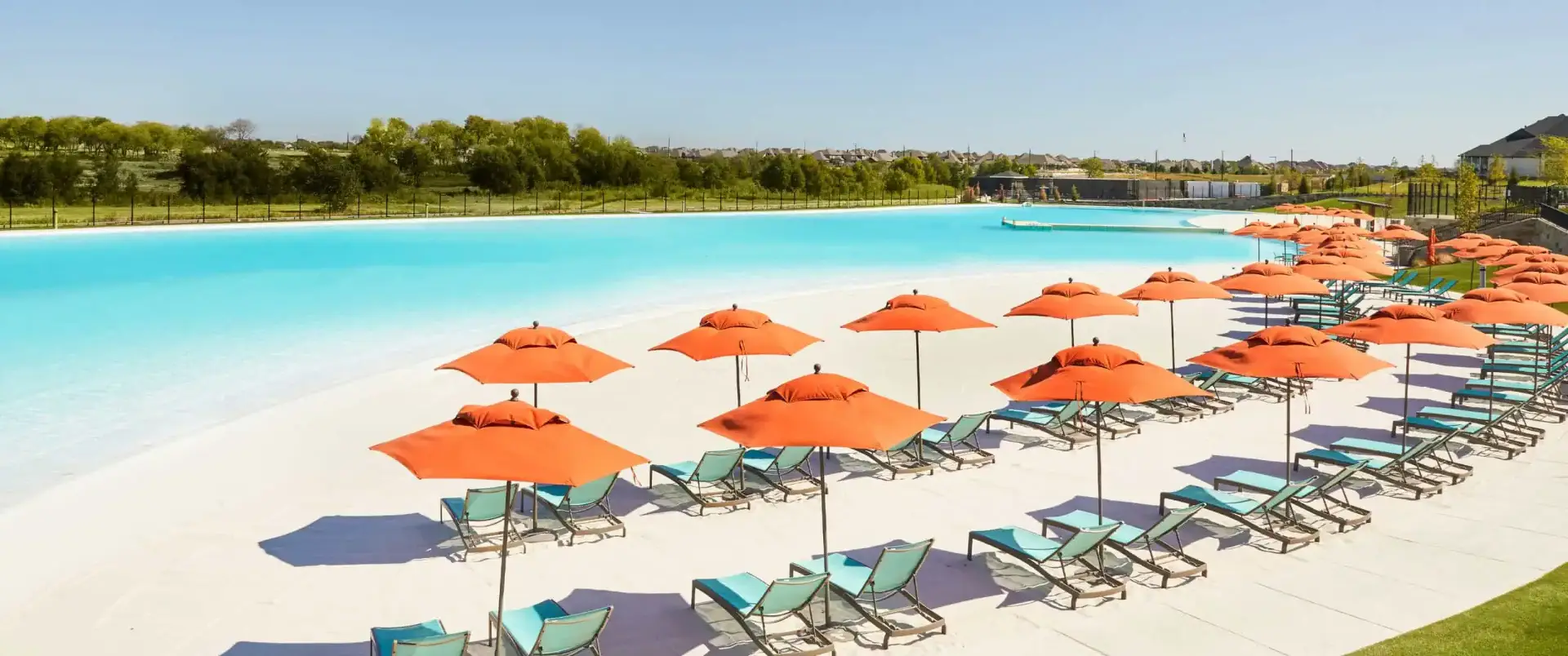 Crystal Lagoon beach at Windsong Ranch with bright orange umbrellas, lounge chairs, and turquoise water under a blue sky