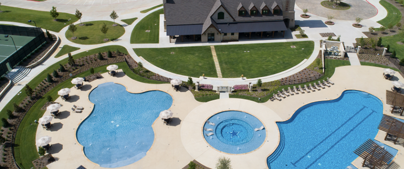 Aerial view of the Star Trail resort-style pools with cabana pergolas, sun shelves, and the stone clubhouse under a bright blue sky